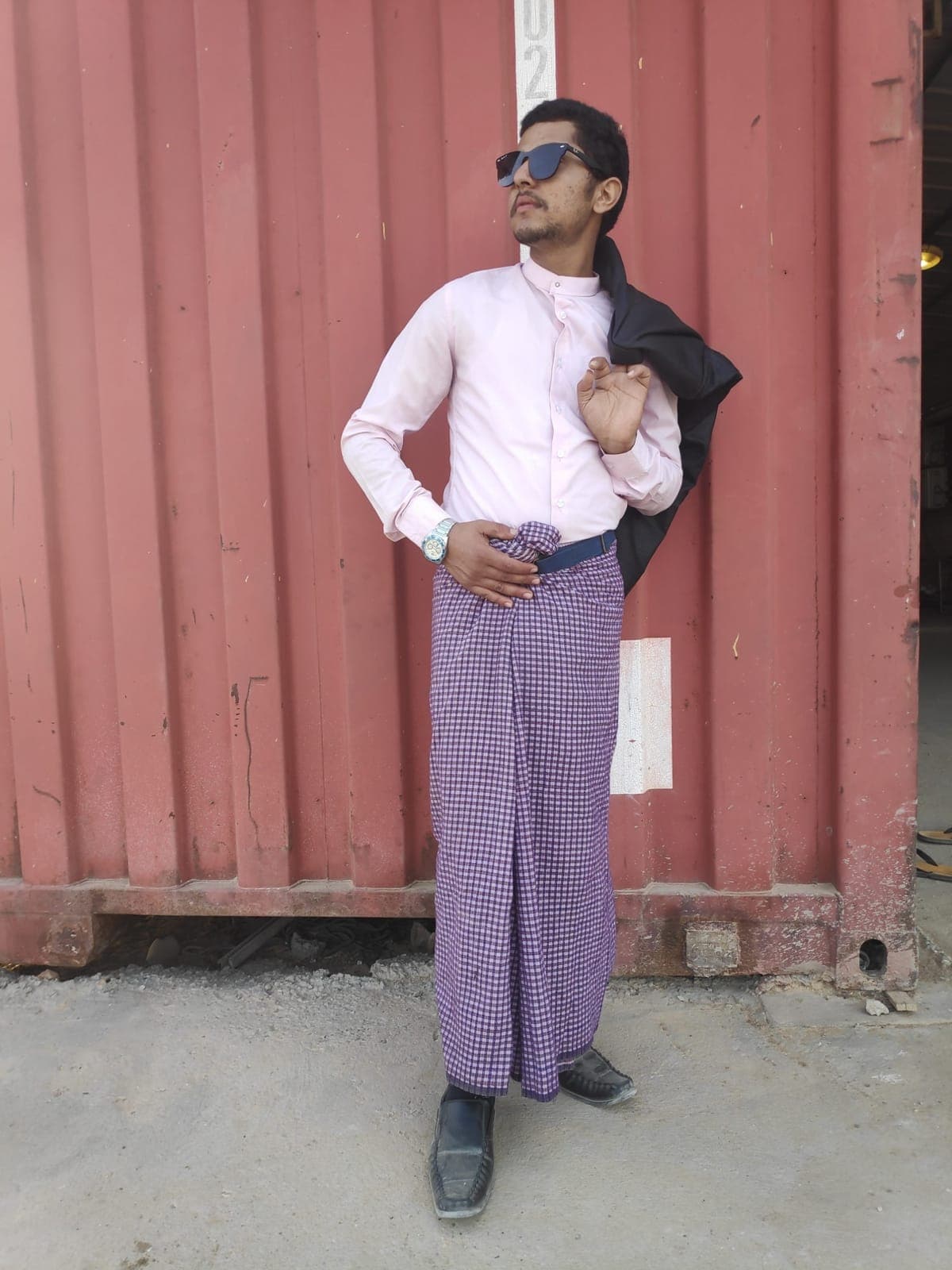 Rabin Paudel in a lungi and sunglasses beside a red shipping container