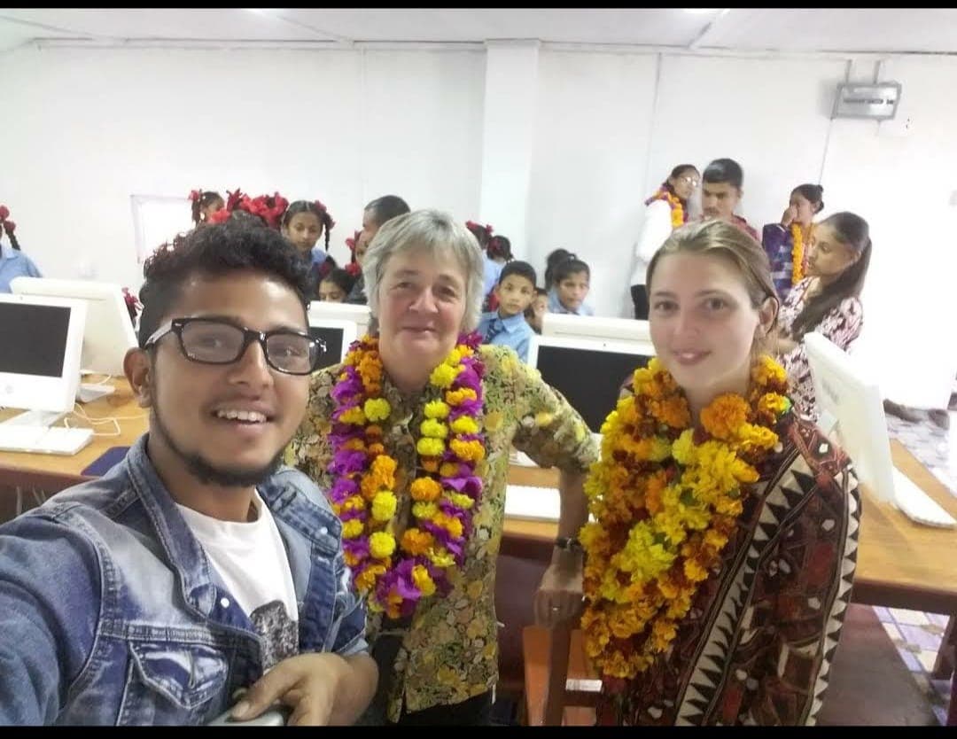 Rabin Paudel with two Danish volunteers wearing marigold garlands in an iMac lab full of students